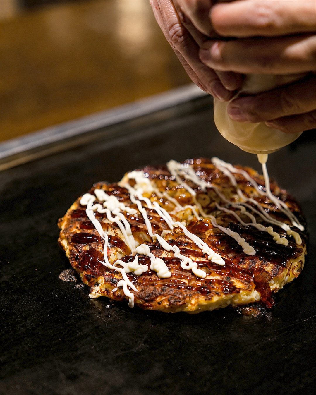 Diners griddling okonomiyaki on the teppan at their table